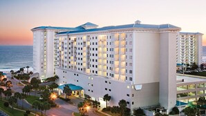 A multi-story hotel with a central courtyard, surrounded by palm trees and a view of the ocean. - Two Bedroom Deluxe Luxury Condo, Destin Florida (1985476) (Destin)