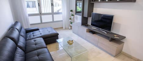 A modern living room with a sectional sofa, a glass coffee table, a flat-screen TV, and a built-in entertainment unit.