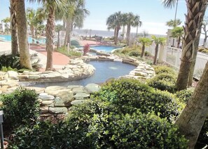 A pool area with a natural rock border, palm trees, and a view of the ocean. - Legacy I 303 (Gulfport)