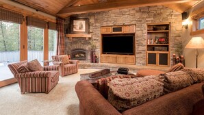 A cozy living room with a stone fireplace, wooden ceiling beams, and a large flat-screen TV. - Sunriver Retreat with Access to The Cove (Sunriver)