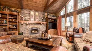 A cozy living room with leather furniture, a stone fireplace, and large windows. - Sunriver Retreat with Access to The Cove (Sunriver)