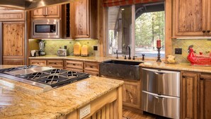 A kitchen with wooden cabinets, stainless steel appliances, a granite countertop, and a window with a view of trees. - Sunriver Retreat with Access to The Cove (Sunriver)