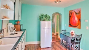 Una cocina compacta con un refrigerador blanco, una mesa de comedor con sillas y paredes color turquesa.