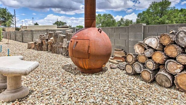 Un entorno rústico al aire libre con una gran estructura metálica oxidada, posiblemente una chimenea o un adorno, rodeada de troncos y grava.