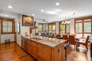 Enjoy meals in the kitchen with a large island and ample counter space, adjacent to a dining area with a wooden table.