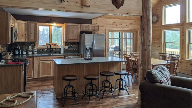 A rustic cabin interior with a wooden kitchen, a dining area, and a bar with stools.