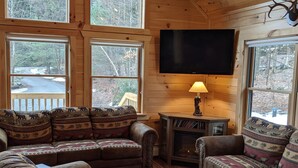 A cozy cabin interior with a large sectional sofa, a television mounted on the wall, and a fireplace.