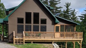 A two-story cabin with a balcony, large windows, and a green roof.