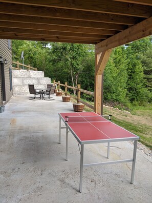 An outdoor patio with a ping pong table, seating area, and stone walls. - Escape to The Adirondack Retreat ~ Gore Skiing & Lake George! (Athol)