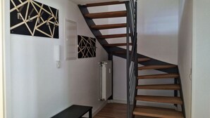 Un escalier avec des marches en bois et une rampe en métal, une œuvre d’art murale géométrique en noir et blanc, un téléphone fixé au mur, et un radiateur.