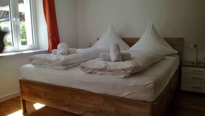 Un lit bien fait, avec du linge de lit blanc et des oreillers, une tête de lit en bois et une table de chevet avec une lampe.