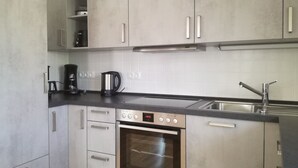 Une cuisine moderne avec des meubles gris, des appareils en acier inoxydable et un plan de travail noir.
