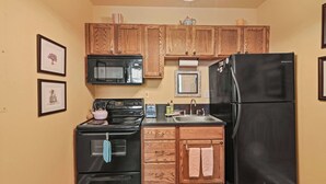 A compact kitchen with wooden cabinets, a black refrigerator, a microwave, an oven, and a sink.