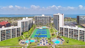 A hotel complex with multiple high-rise buildings, a central pool area, and tennis courts. - Quaint Beachfront Condo with Resort Pools, Hot Tubs, Tennis Courts & More! (South Padre Island)