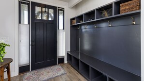 Un hall d’entrée moderne avec une porte en bois foncé, un banc muni de patères et une étagère avec des paniers et des objets décoratifs.