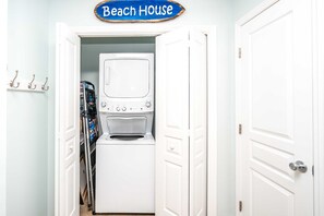 Un lavadero con lavadora y secadora, un tendedero con ropa doblada, y un cartel que dice 'Beach House'.