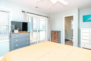 Un dormitorio con cama, televisor sobre una cómoda, puerta corrediza de vidrio y un baño visible a través de una puerta abierta.