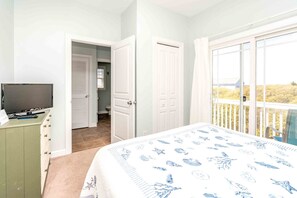 A bedroom with a bed, a television on a dresser, and a balcony with a view. - Beaches B Tripp'n - Awesome 4 BR Home - Ocean View and Elevator! (North Topsail Beach)
