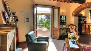 A spacious living room with a leather armchair, a wooden coffee table with a vase of flowers, and a view of a garden through an open door.