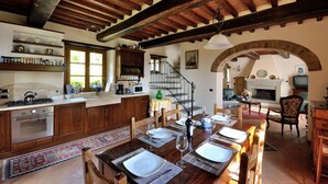 A rustic kitchen with wooden cabinets, a dining area with a table set for two, and a fireplace in the background.