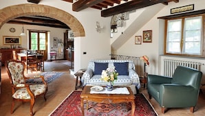 A spacious living room with a high ceiling, exposed wooden beams, a large arched doorway, and a view of a dining area.