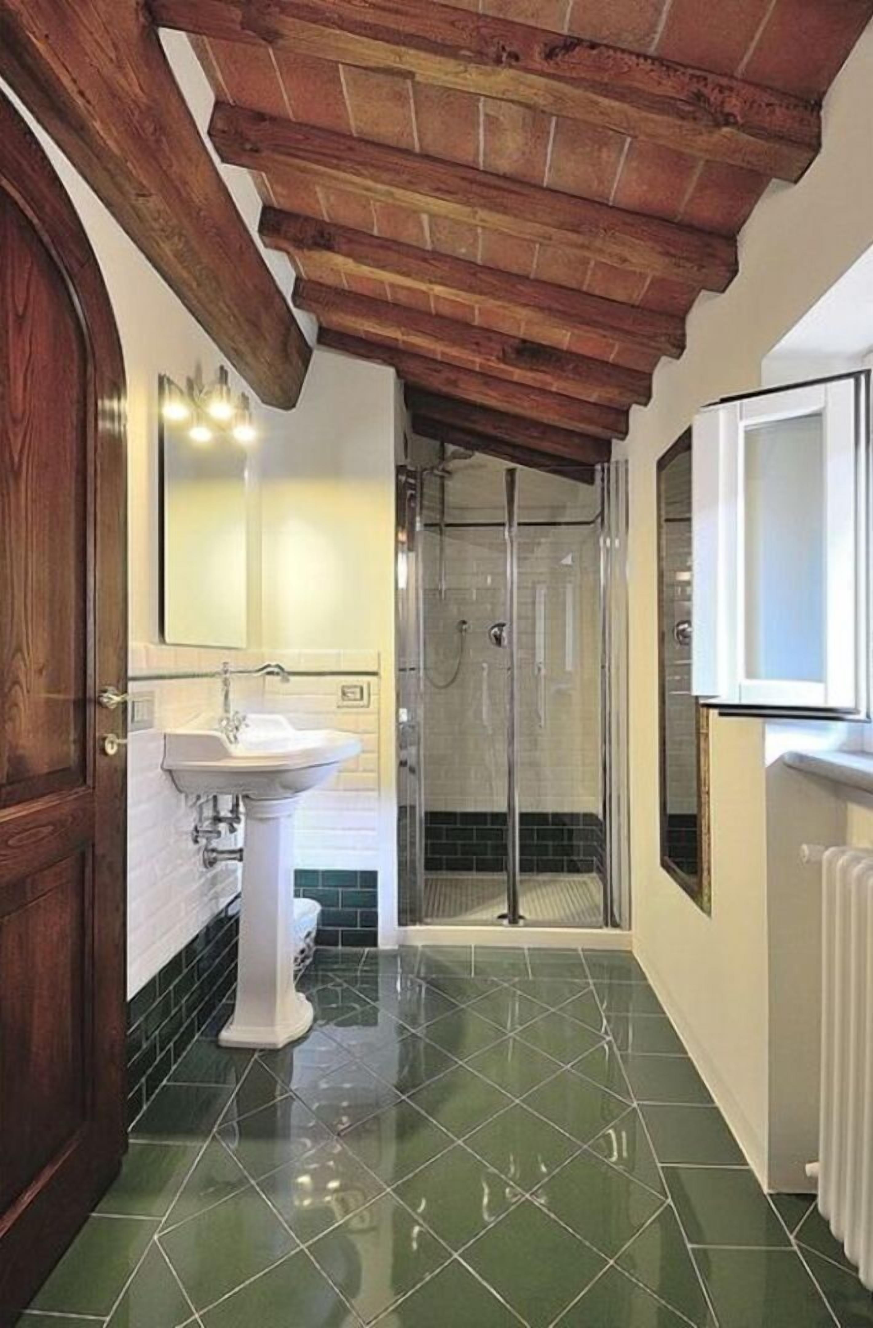 Een badkamer met een wastafel op een voetstuk, een douchecabine van glas en een houten plafond.