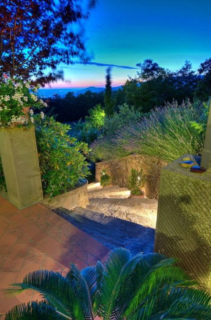 A garden pathway leading to a stone structure with a view of the sea at dusk.