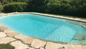 Une piscine rectangulaire à l’eau d’un bleu limpide, entourée de carreaux de pierre et bordée d’une margelle en pierre.