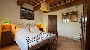 Une chambre à coucher avec un lit, deux tables de chevet avec des lampes, une porte en bois, un miroir et un luminaire suspendu.