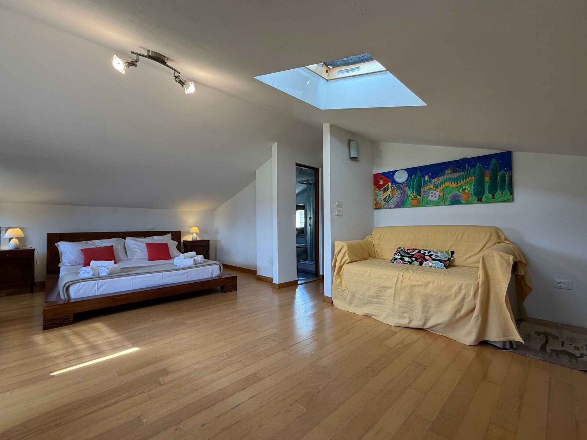 Une chambre à coucher avec un lit, un canapé, une lucarne et un tableau au mur.