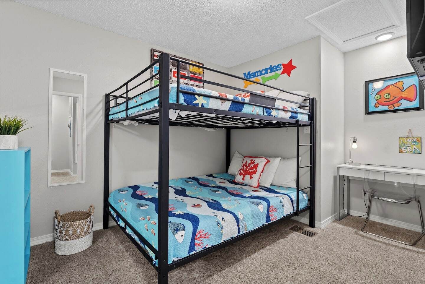 Habitación con literas, una colcha azul y blanca con motivos náuticos, un escritorio pequeño con silla, un televisor montado en la pared y un cuadro con un pez.