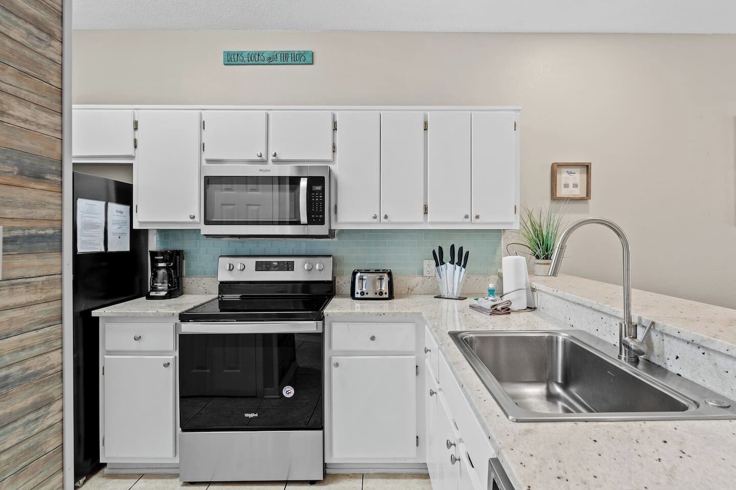 A modern kitchen with white cabinets, a stainless steel sink, a microwave, a stove, and a toaster.