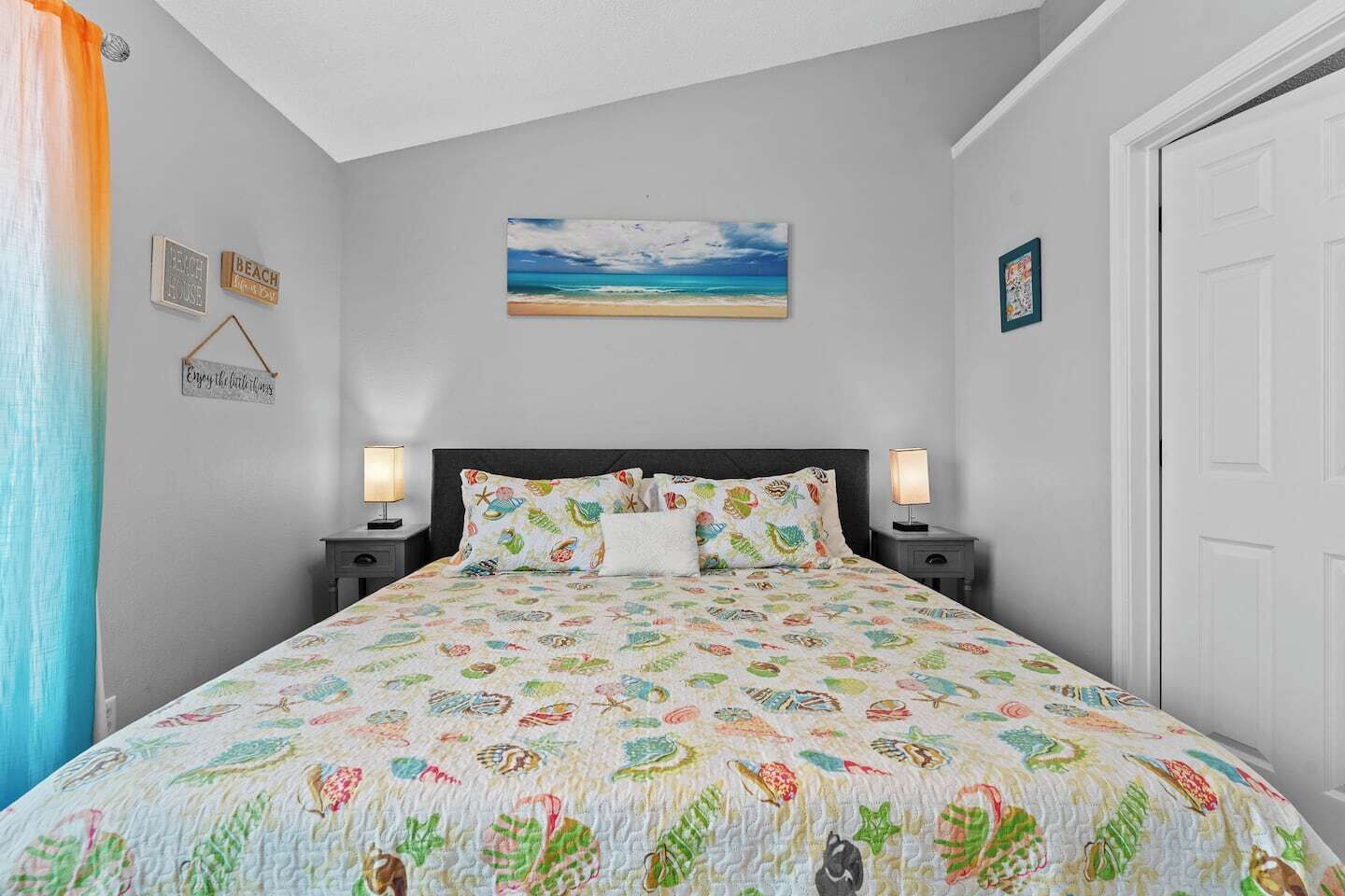 Une chambre à coucher comprenant un lit, deux tables de chevet, une commode, une porte et un mur orné d’un tableau et de quelques affiches.