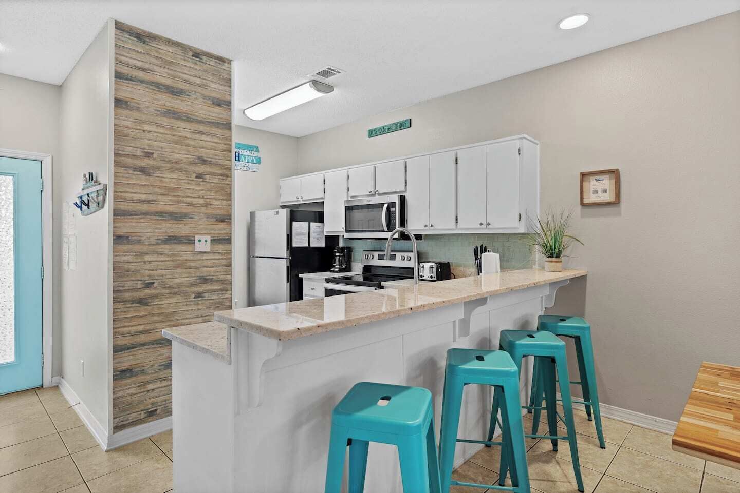 A modern kitchen with white cabinets, a central island with bar stools, a microwave, and a refrigerator.