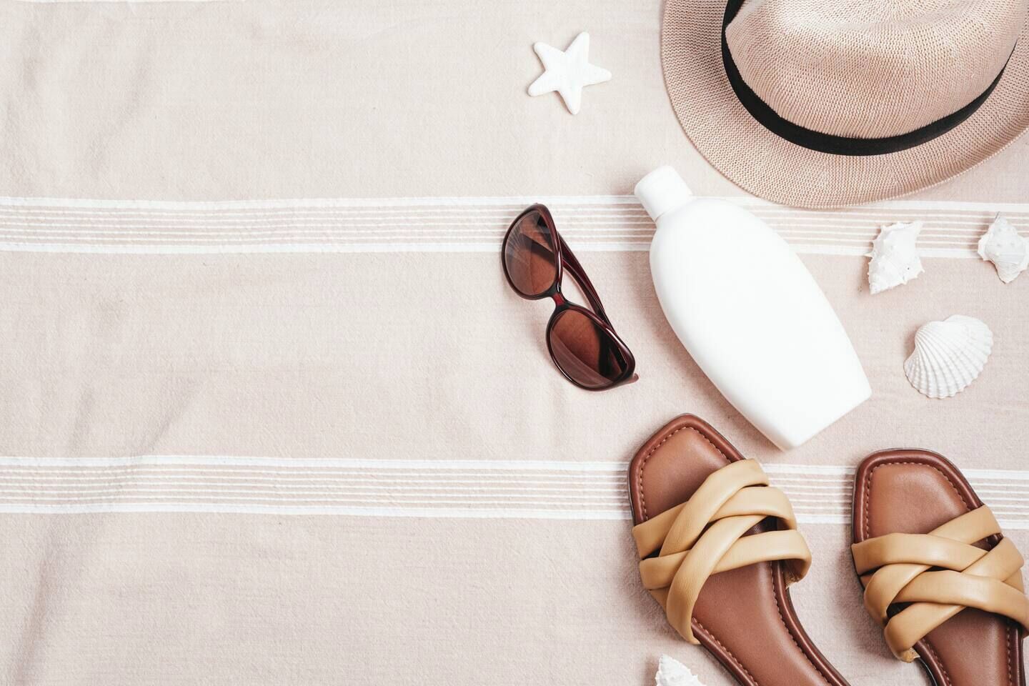 A beach towel with a pair of sandals, a bottle, sunglasses, and a straw hat.