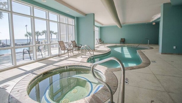 An indoor swimming pool area with multiple pools, sun loungers, and large windows offering a view of the beach. - Legacy II 1408 Penthouse (Gulfport)