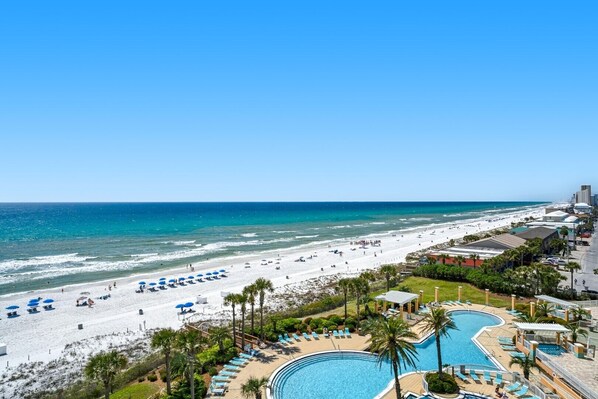 A beach resort with a swimming pool, beach umbrellas, and a view of the ocean.