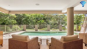Zona de piscina con mobiliario de mimbre y vistas al follaje circundante.