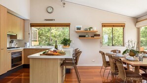 Una cocina moderna con una isla central, armarios de madera y un comedor con sillas de mimbre y una mesa preparada para dos.
