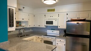 Una cucina con mobili bianchi, un piano di lavoro in granito, un forno a microonde, un fornello e un frigorifero.