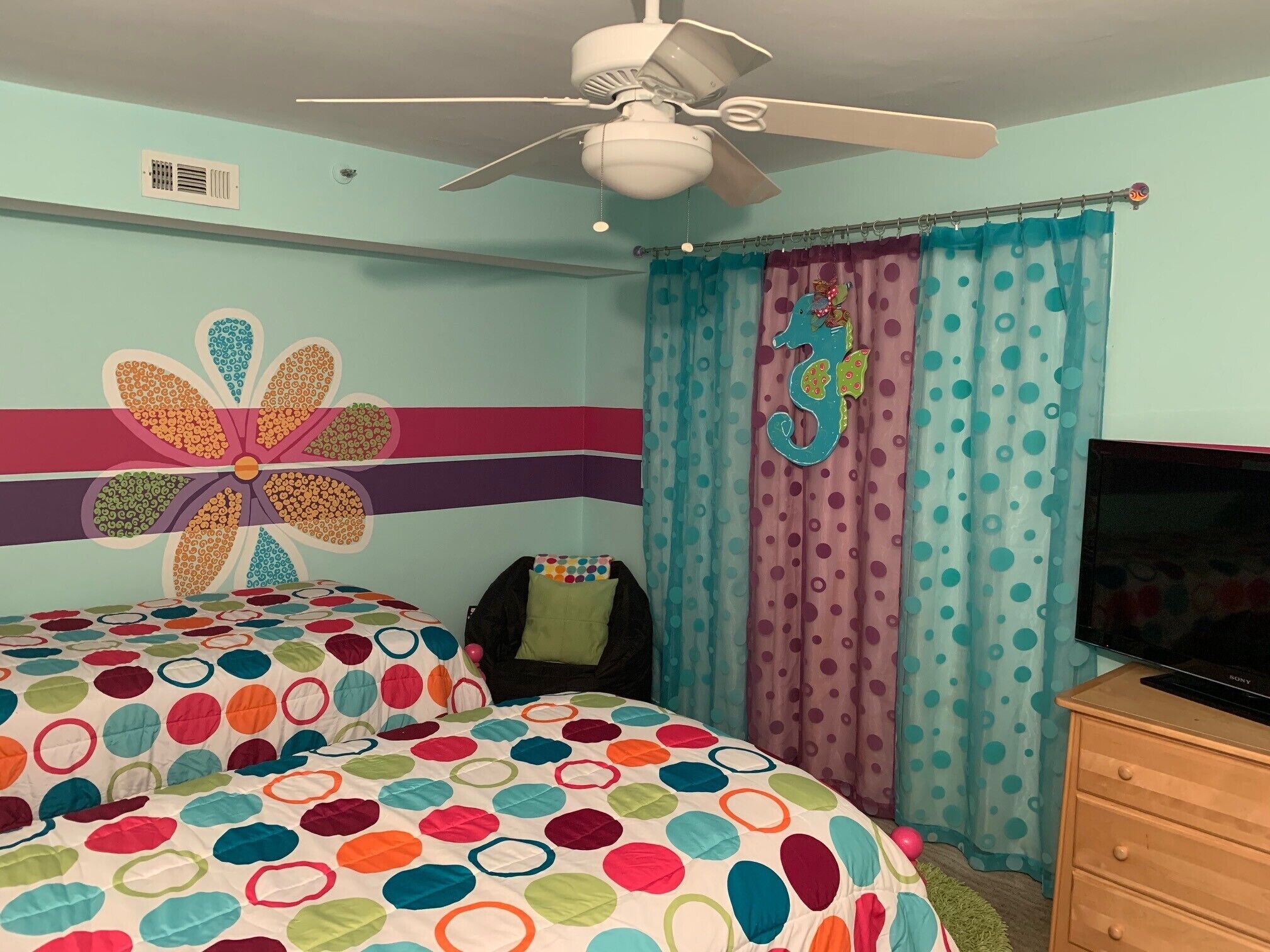 Een slaapkamer met twee bedden, een plafondventilator, een televisie en een dressoir.