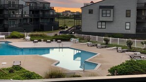 Una piscina con lettini e un recinto bianco, circondata da edifici a più piani con balconi.