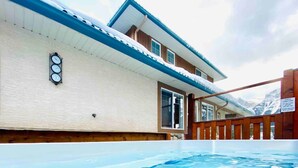 A swimming pool adjacent to a building with a wooden deck and a mountain backdrop. - PRIVATE Entrance, Mountain View ,2 BR/1.5 BT  (Harvie Heights)