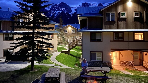 A lodge with a fire pit and picnic table in the yard, surrounded by buildings and mountains. - PRIVATE Entrance, Mountain View ,2 BR/1.5 BT  (Harvie Heights)