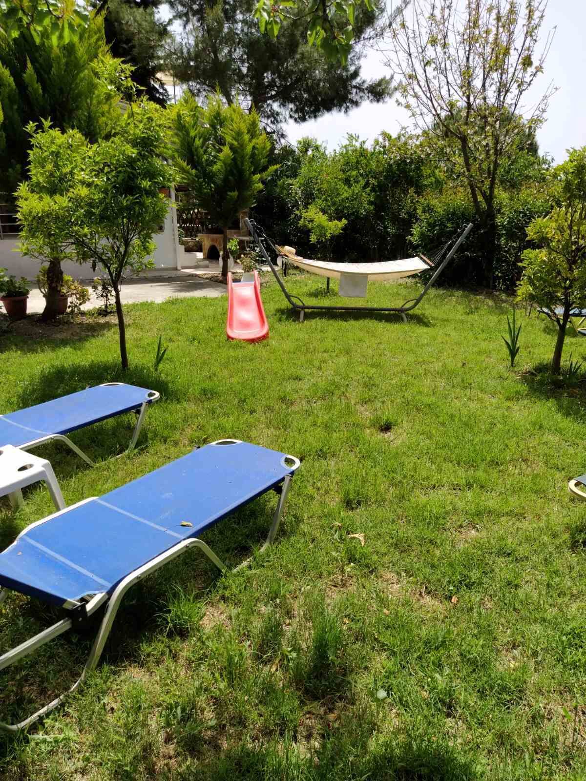 A grassy outdoor area with a hammock, a red slide, and two blue sun loungers.