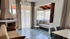 A modern living room with a sofa, a dining table, and a fireplace. - Julia Holiday Apartments (Zakynthos)