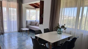 A dining area with a white table and black chairs, a sofa with cushions, and a vase with flowers on the table. - Julia Holiday Apartments (Zakynthos)