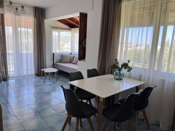 A dining area with a white table and black chairs, a sofa with cushions, and a vase with flowers on the table.