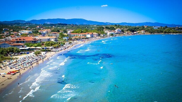 A coastal town with a beach, buildings, and mountains in the background. - Julia Holiday Apartments (Zakynthos)