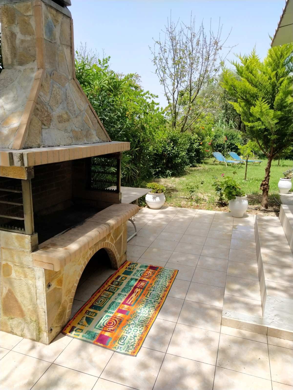 An outdoor stone barbecue area with a tiled patio and a colorful rug.
